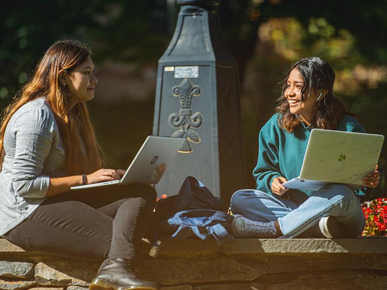 Two students sitting and talking near the campus railroad clock